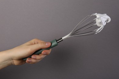 Woman holding whisk with whipped cream on grey background, closeup