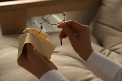 Photo of Woman cleaning glasses with cloth indoors, closeup