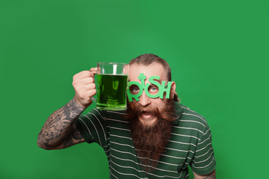 Bearded man in party glasses with green beer on color background. St. Patrick's Day celebration