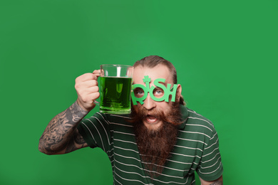 Photo of Bearded man in party glasses with green beer on color background. St. Patrick's Day celebration