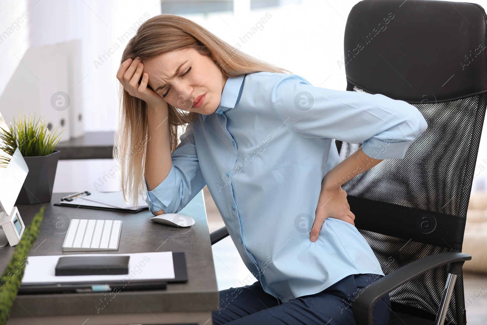 Photo of Young woman suffering from back pain in office