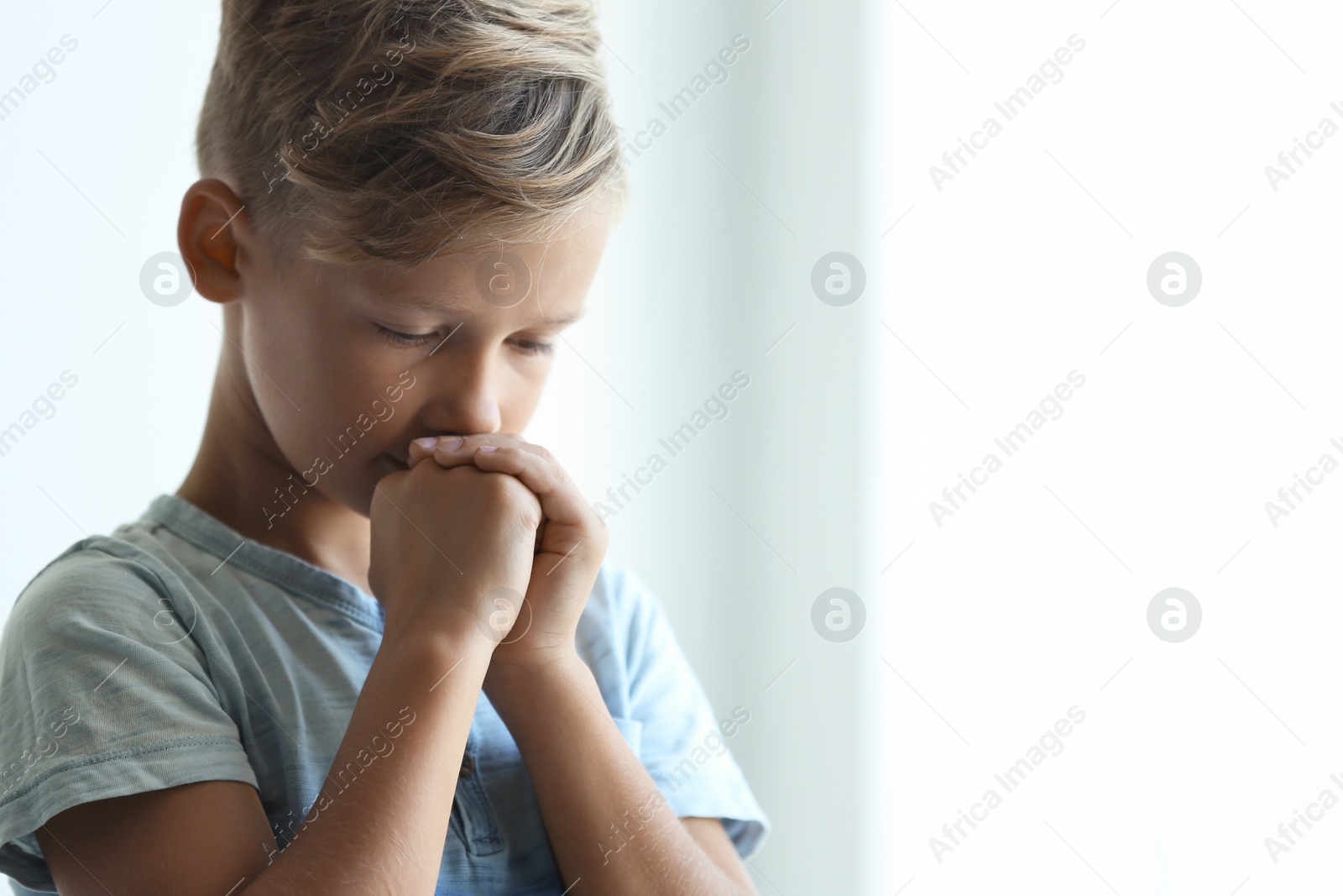 Photo of Little boy with hands clasped together for prayer on light background. Space for text