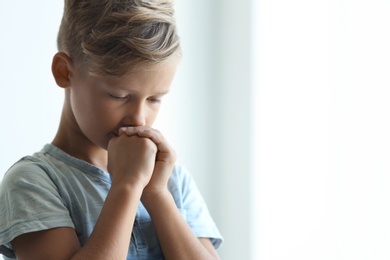 Little boy with hands clasped together for prayer on light background. Space for text