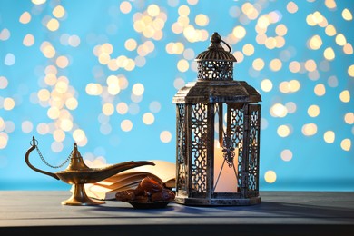 Arabic lantern, Quran, dates and Aladdin magic lamp on table against light blue background with blurred lights
