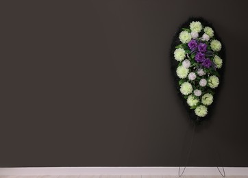 Photo of Funeral wreath of plastic flowers hanging on dark grey wall, space for text