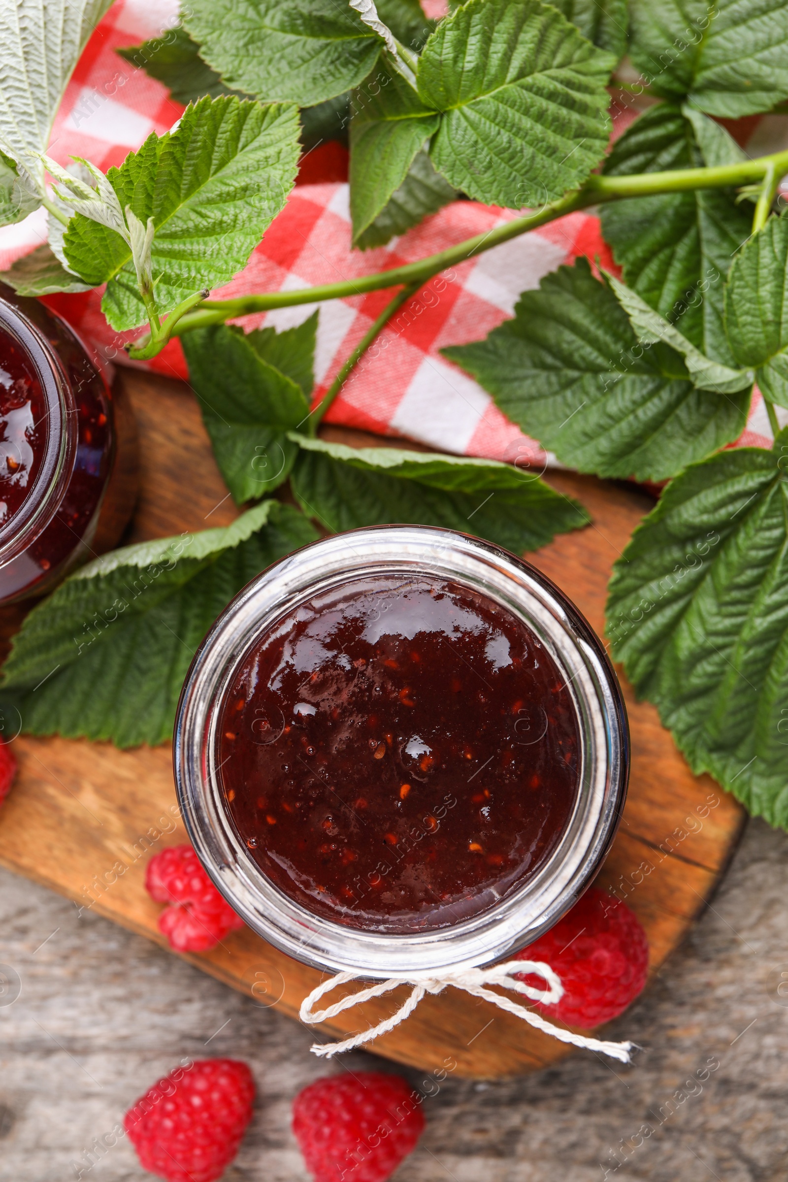 Photo of Delicious raspberry jam, fresh berries and green leaves on wooden table, flat lay