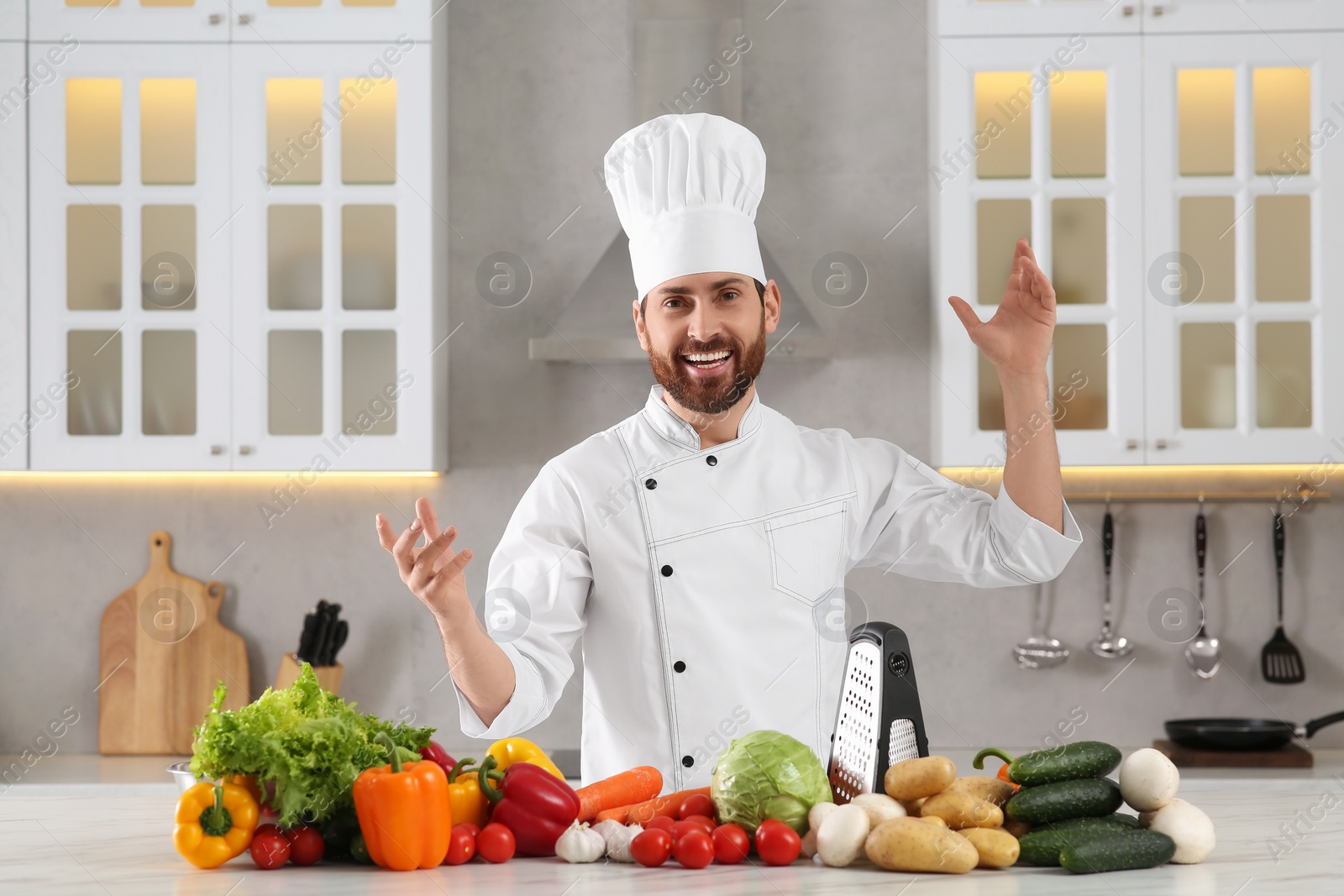 Photo of Happy chef having fun near vegetables at marble table in kitchen