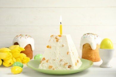 Photo of Traditional cottage cheese Easter paskha with dried apricot and burning candle on white wooden table