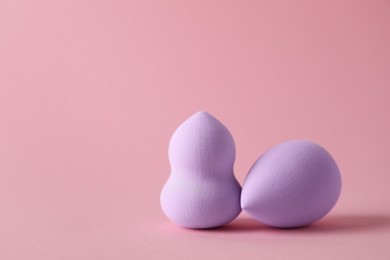 Two violet makeup sponges on pink background, space for text