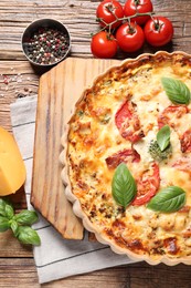 Photo of Tasty quiche with tomatoes, basil and cheese served on wooden table, flat lay