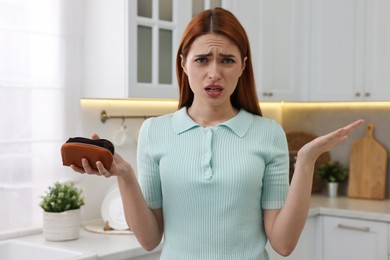 Confused woman with empty wallet at home