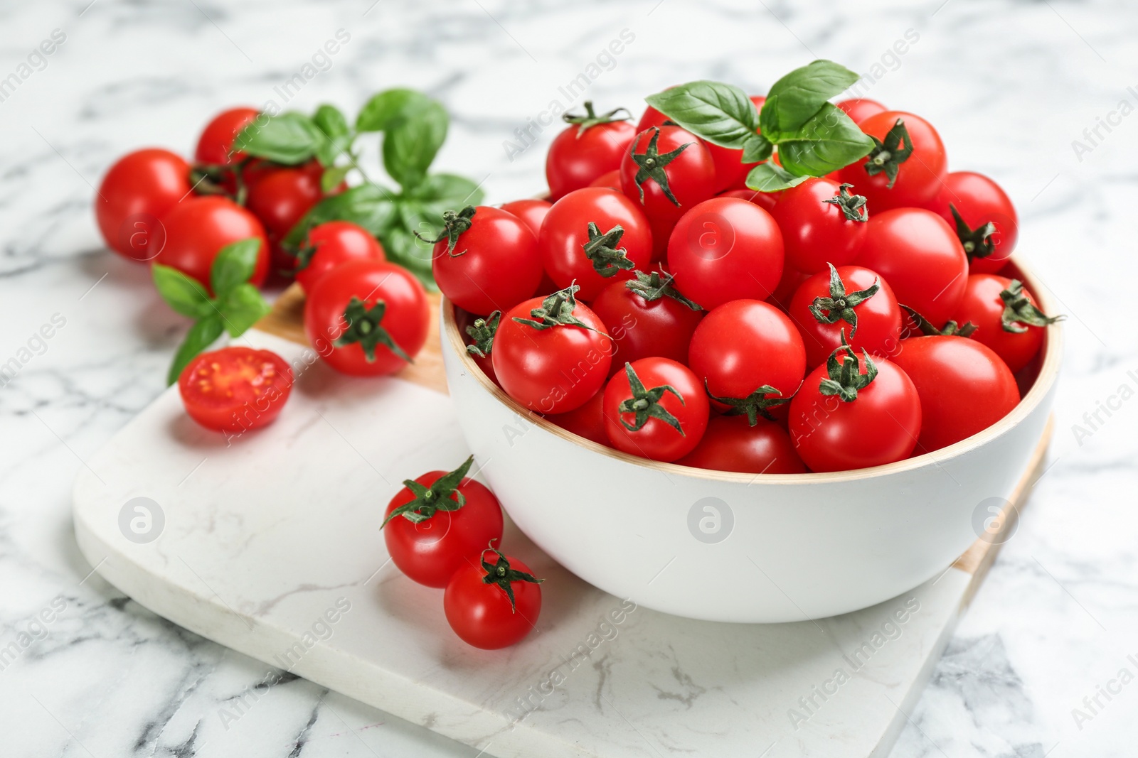 Photo of Fresh cherry tomatoes and basil leaves on white marble table