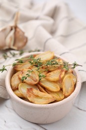 Photo of Fried garlic cloves and thyme in bowl on white table, closeup