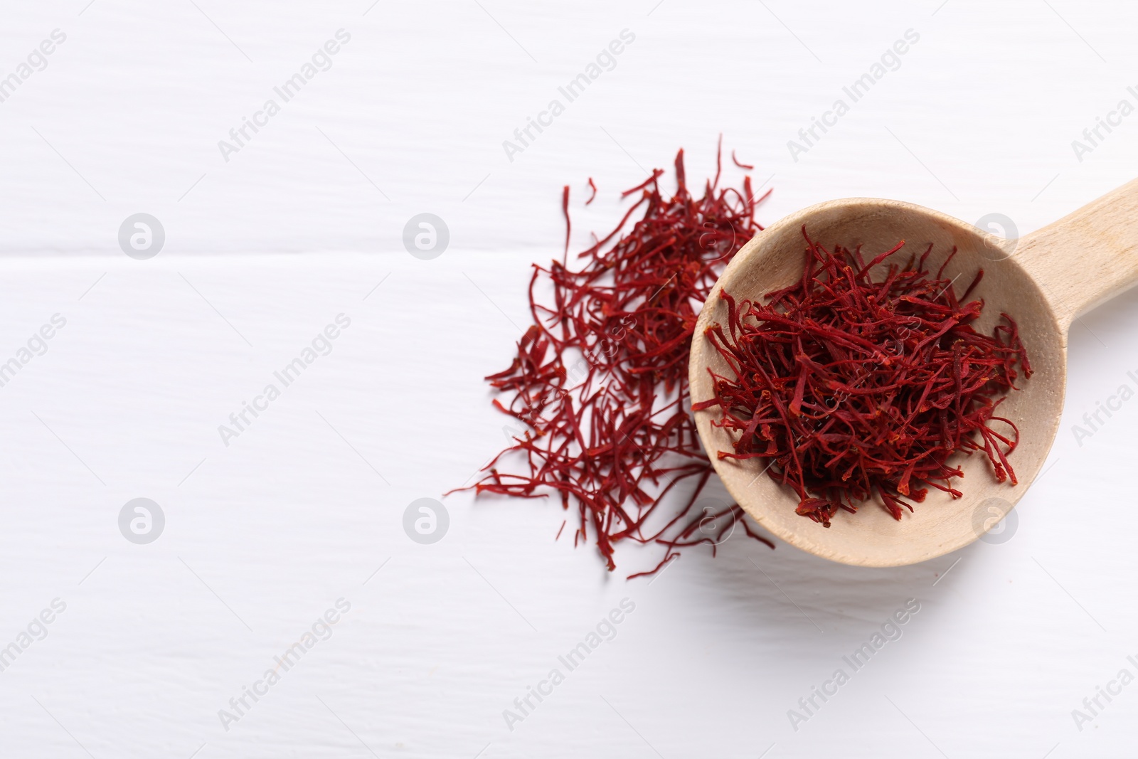 Photo of Aromatic saffron and spoon on white wooden table, top view. Space for text