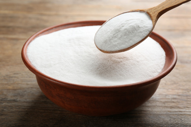 Photo of Baking soda in spoon and bowl on wooden table, closeup