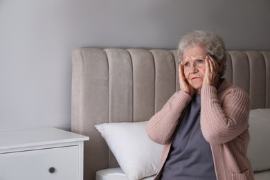 Photo of Senior woman with headache in bedroom at home. Space for text