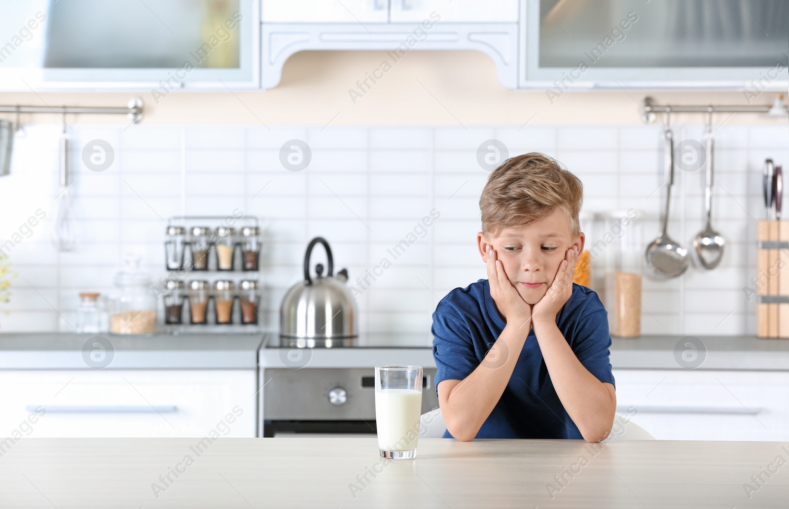 Photo of Adorable little boy with glass of milk in kitchen