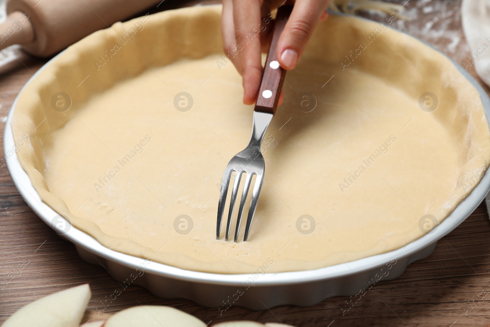 Photo of Woman making holes in raw dough with fork at wooden table, closeup. Baking apple pie