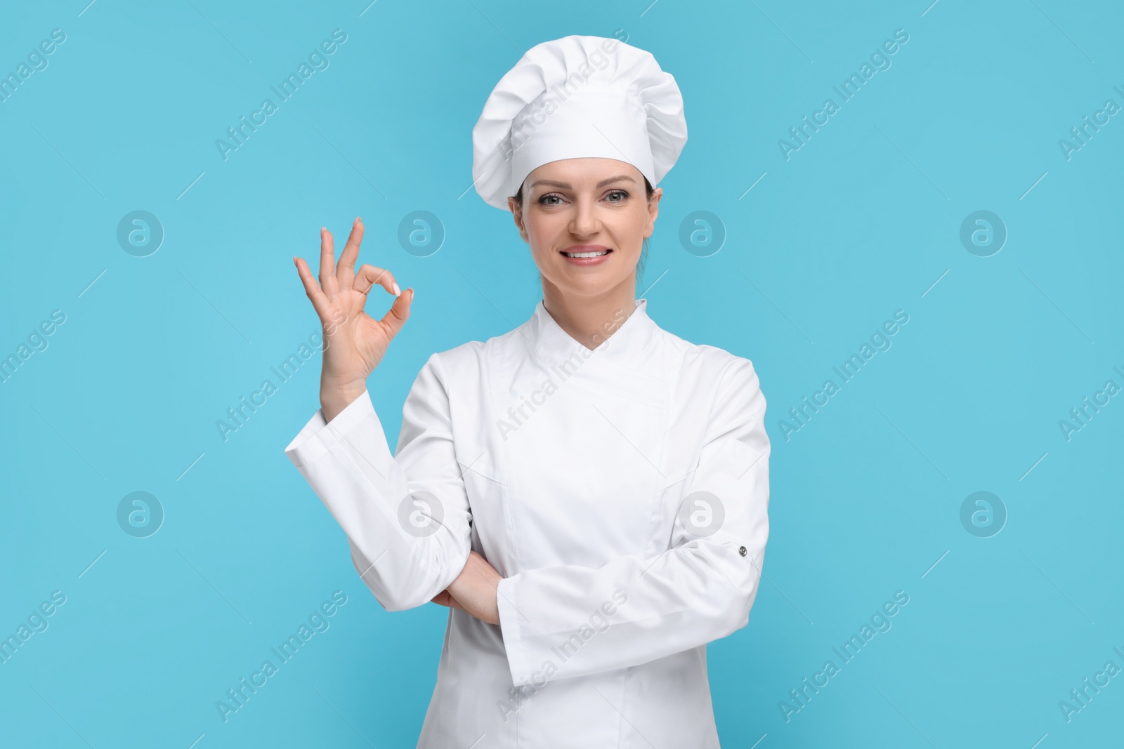 Photo of Happy woman chef in uniform showing OK gesture on light blue background