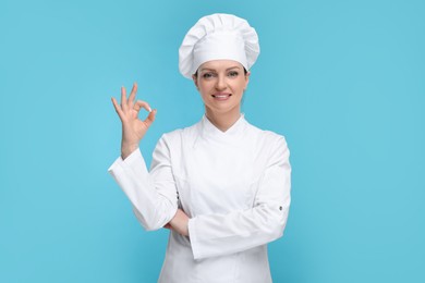 Photo of Happy woman chef in uniform showing OK gesture on light blue background