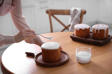 Young woman decorating traditional Easter cake with glaze in kitchen, closeup. Space for text