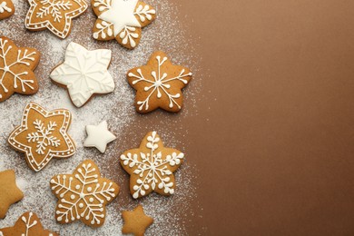 Tasty Christmas cookies with icing and powdered sugar on brown background, flat lay. Space for text