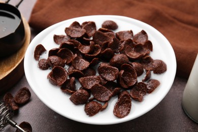 Photo of Breakfast cereal. Chocolate corn flakes and milk in bowl on brown table, closeup