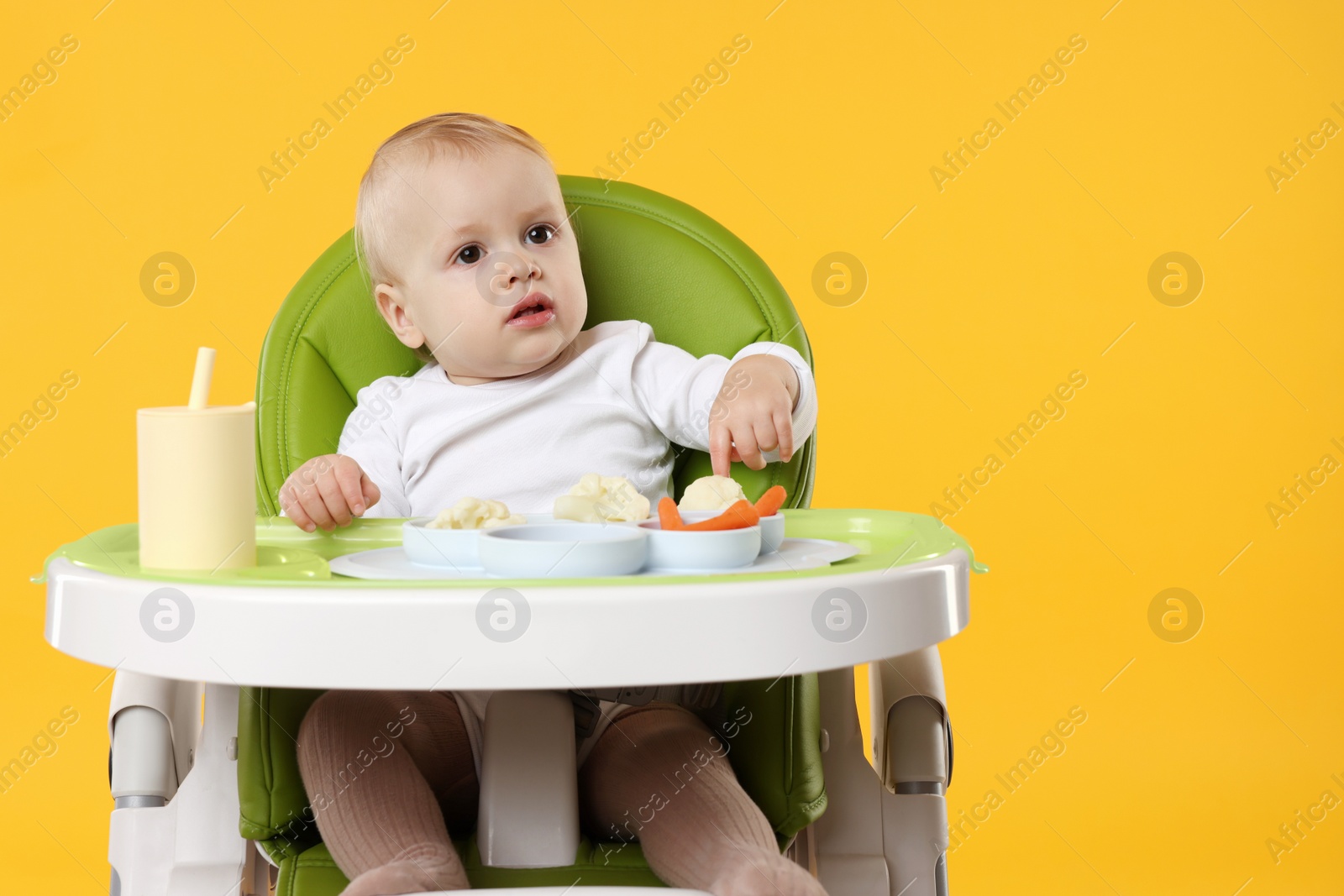 Photo of Cute little baby with healthy food in high chair on orange background, space for text