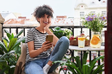 Beautiful young woman using smartphone at table on balcony with houseplants