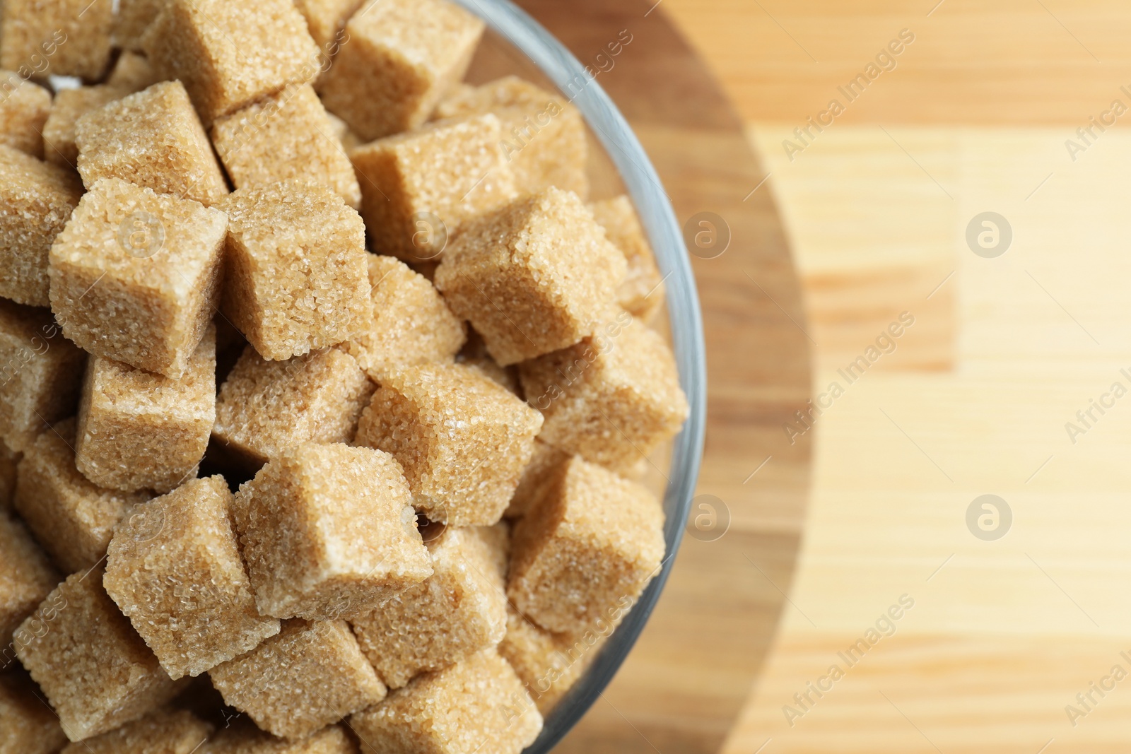 Photo of Brown sugar cubes in bowl on wooden table, top view