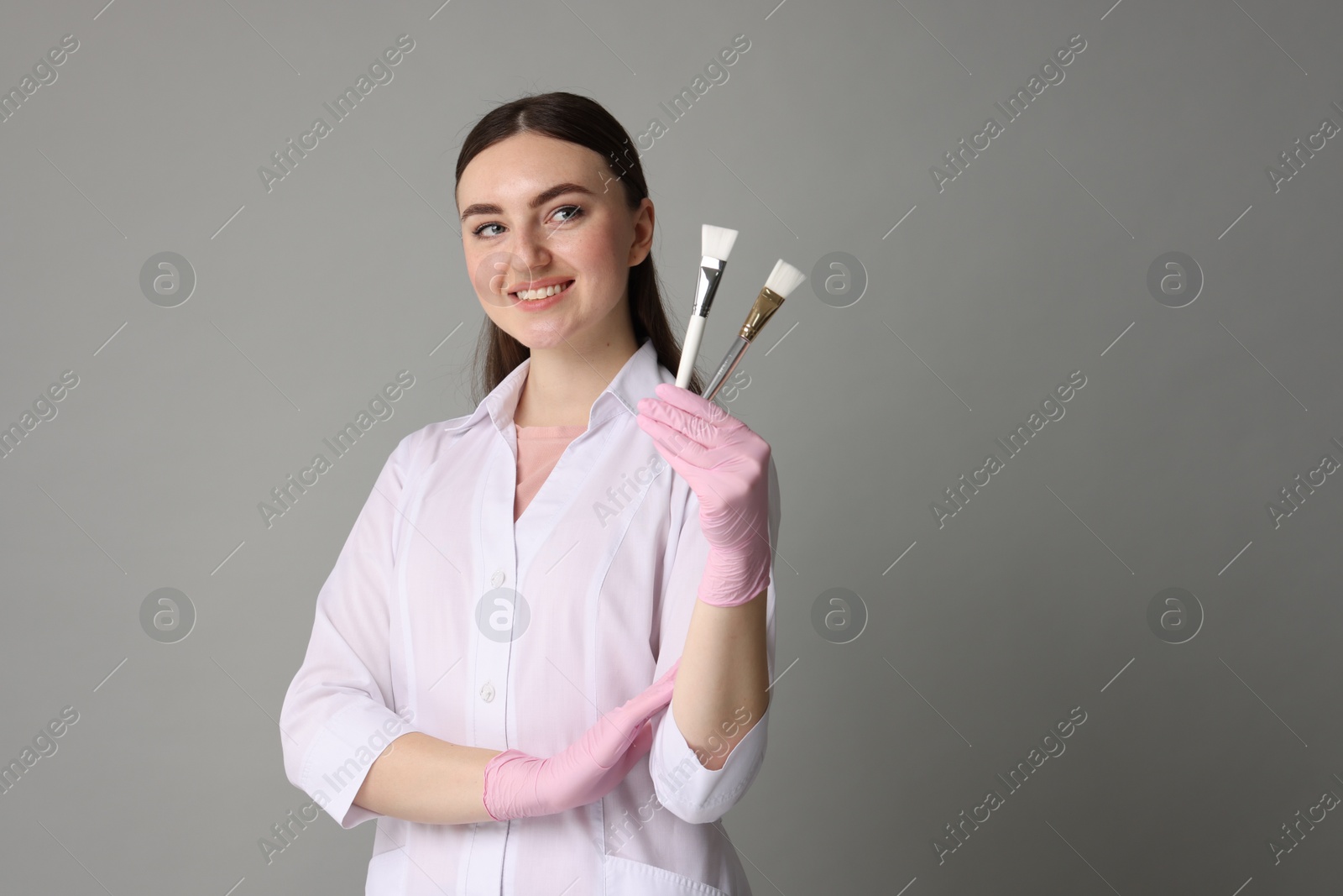 Photo of Cosmetologist with cosmetic brushes on grey background, space for text