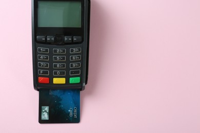 New modern payment terminal with credit card on pink background, top view. Space for text