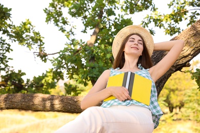 Photo of Young woman reading book on tree in park