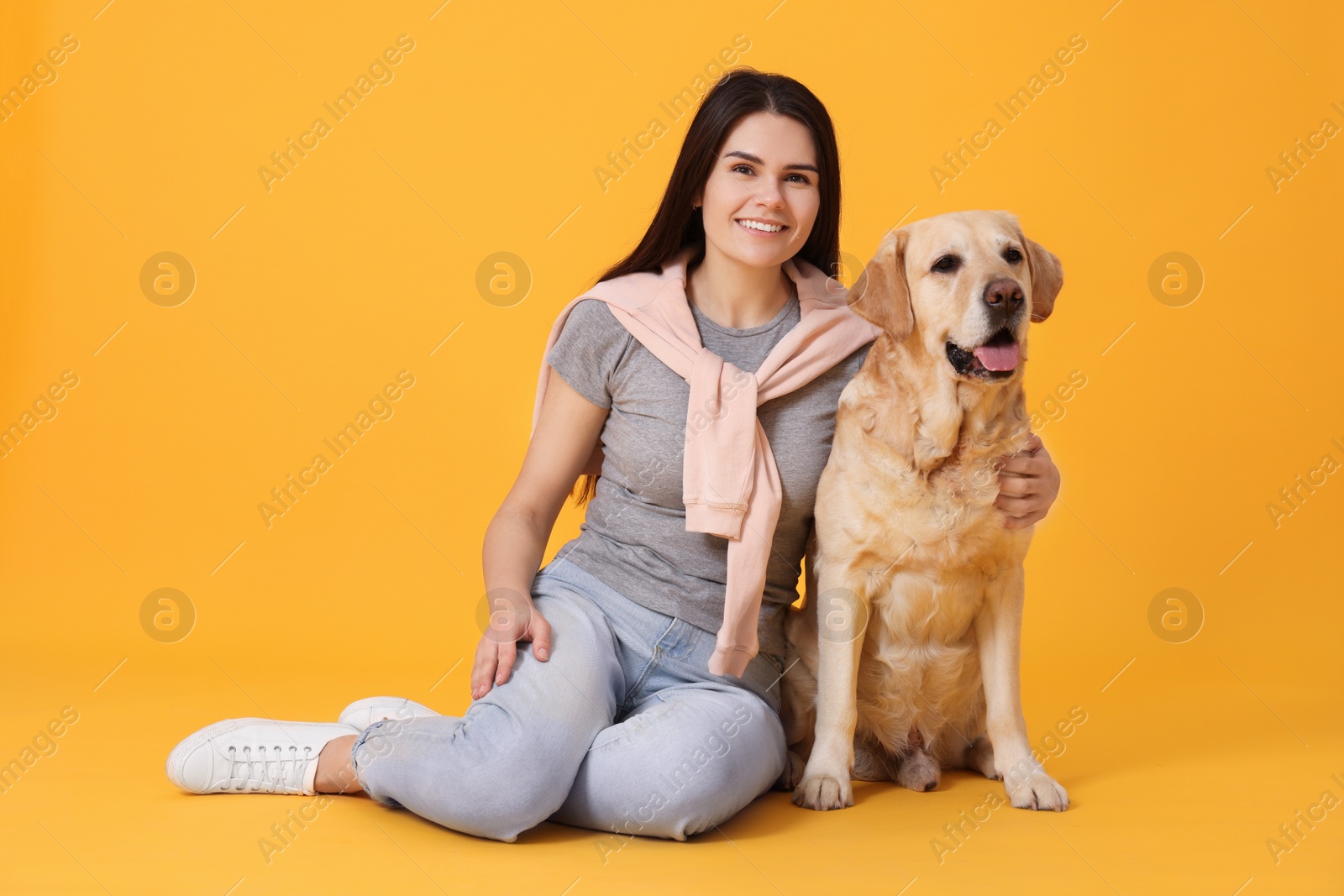 Photo of Portrait of happy woman with cute Labrador Retriever on orange background