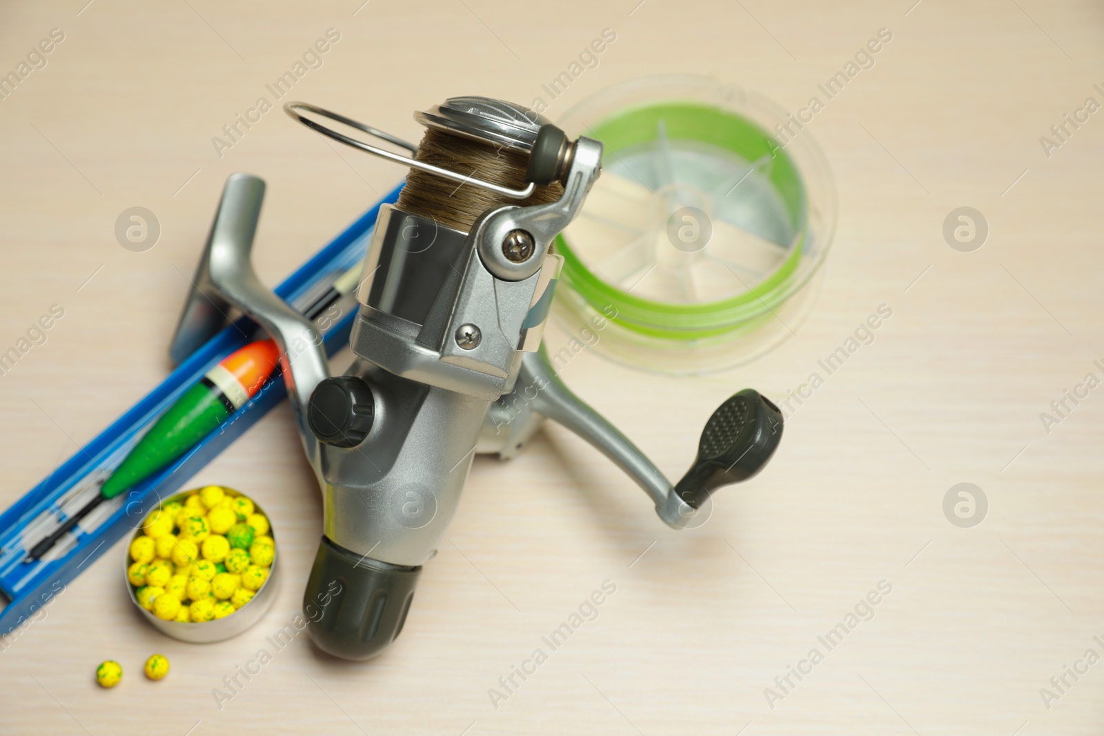 Photo of Reel with fishing line and other equipment on light wooden table. Space for text