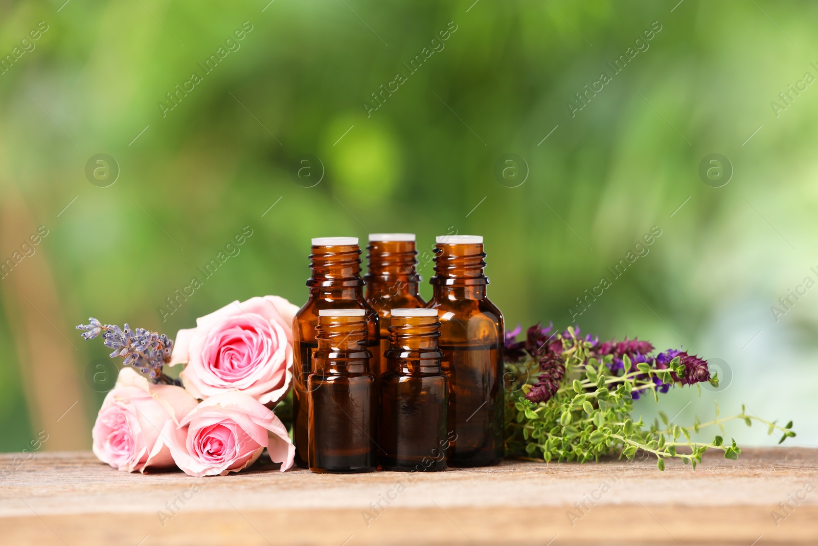 Photo of Bottles with essential oils, herbs and flowers on wooden table against blurred green background. Space for text