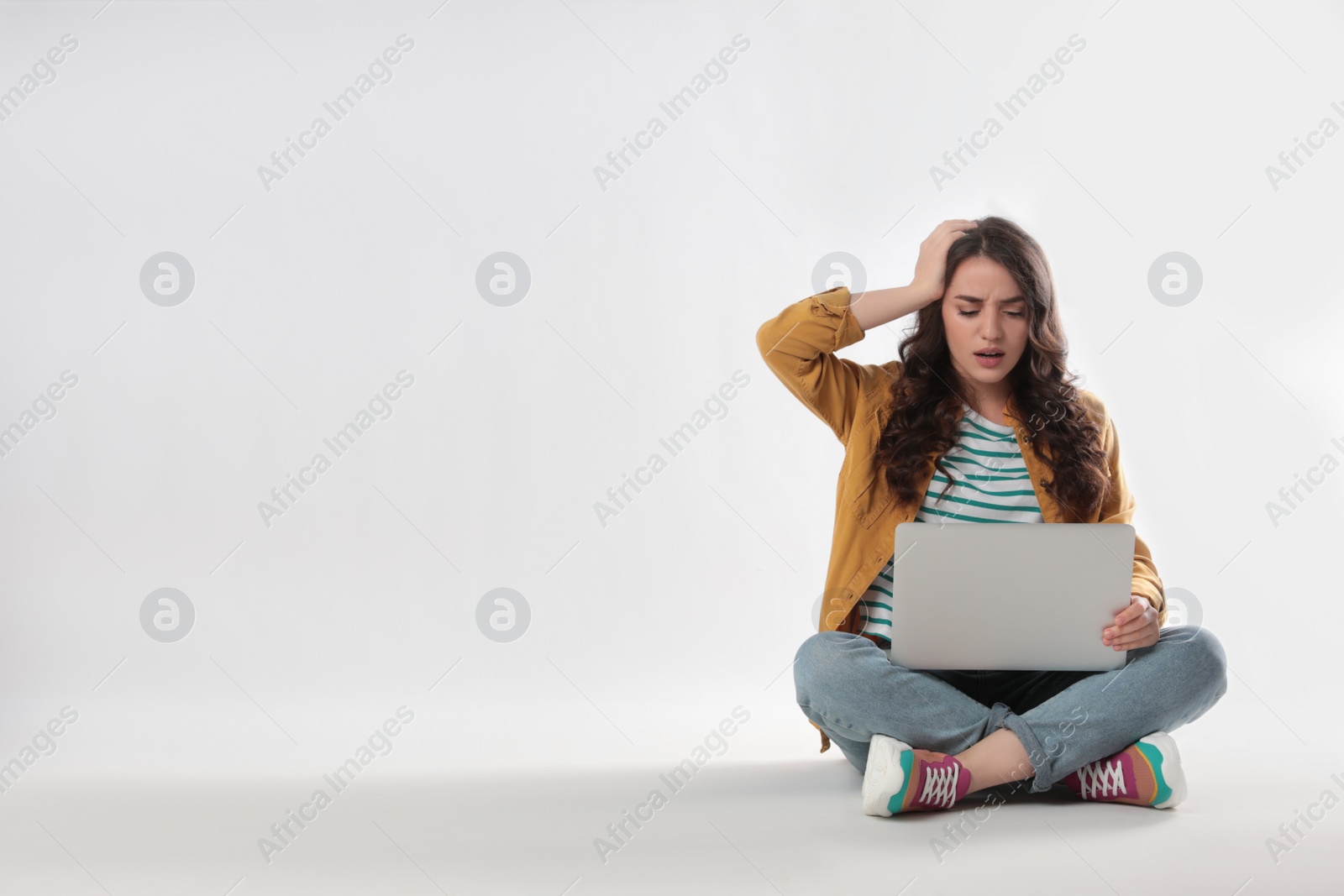 Photo of Shocked young woman sitting with laptop on white background