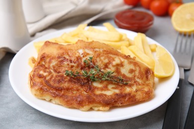 Tasty soda water battered fish, potato chips and lemon slice on light grey table