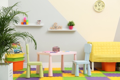 Photo of Stylish playroom interior with table, chairs and sofa
