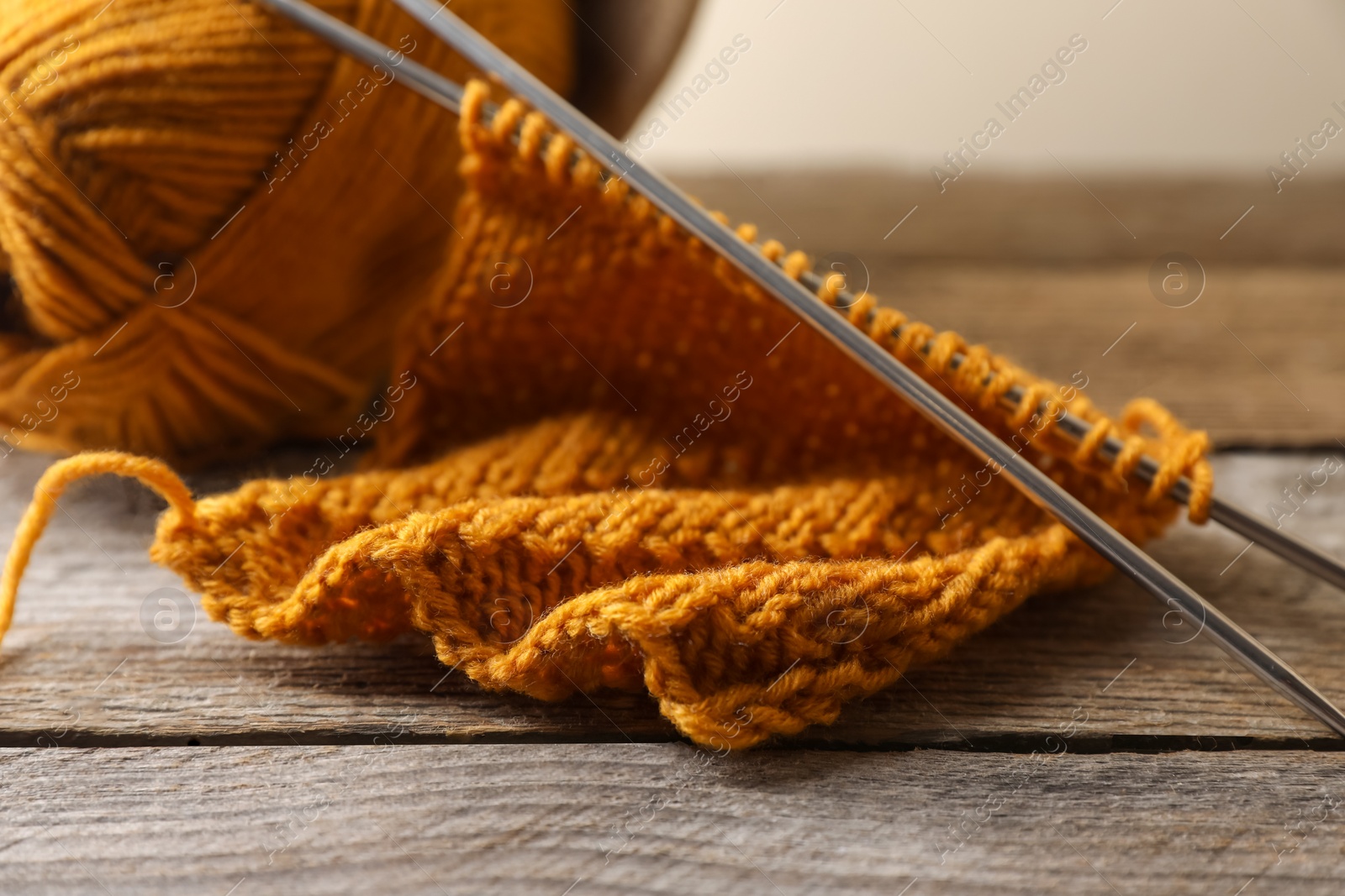 Photo of Soft orange knitting, yarn and metal needles on wooden table, closeup