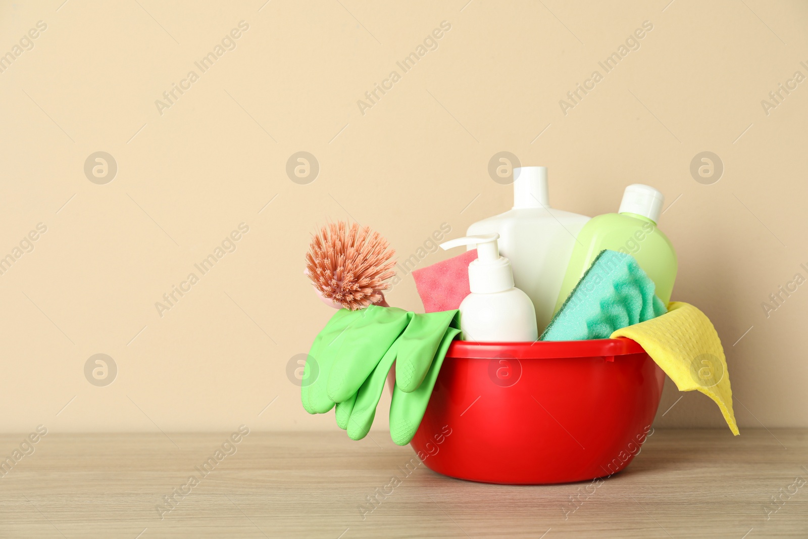 Photo of Basin with different cleaning supplies on wooden floor near beige wall. Space for text