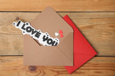 Photo of Sheet of paper with phrase I Love You and envelopes on wooden table, flat lay
