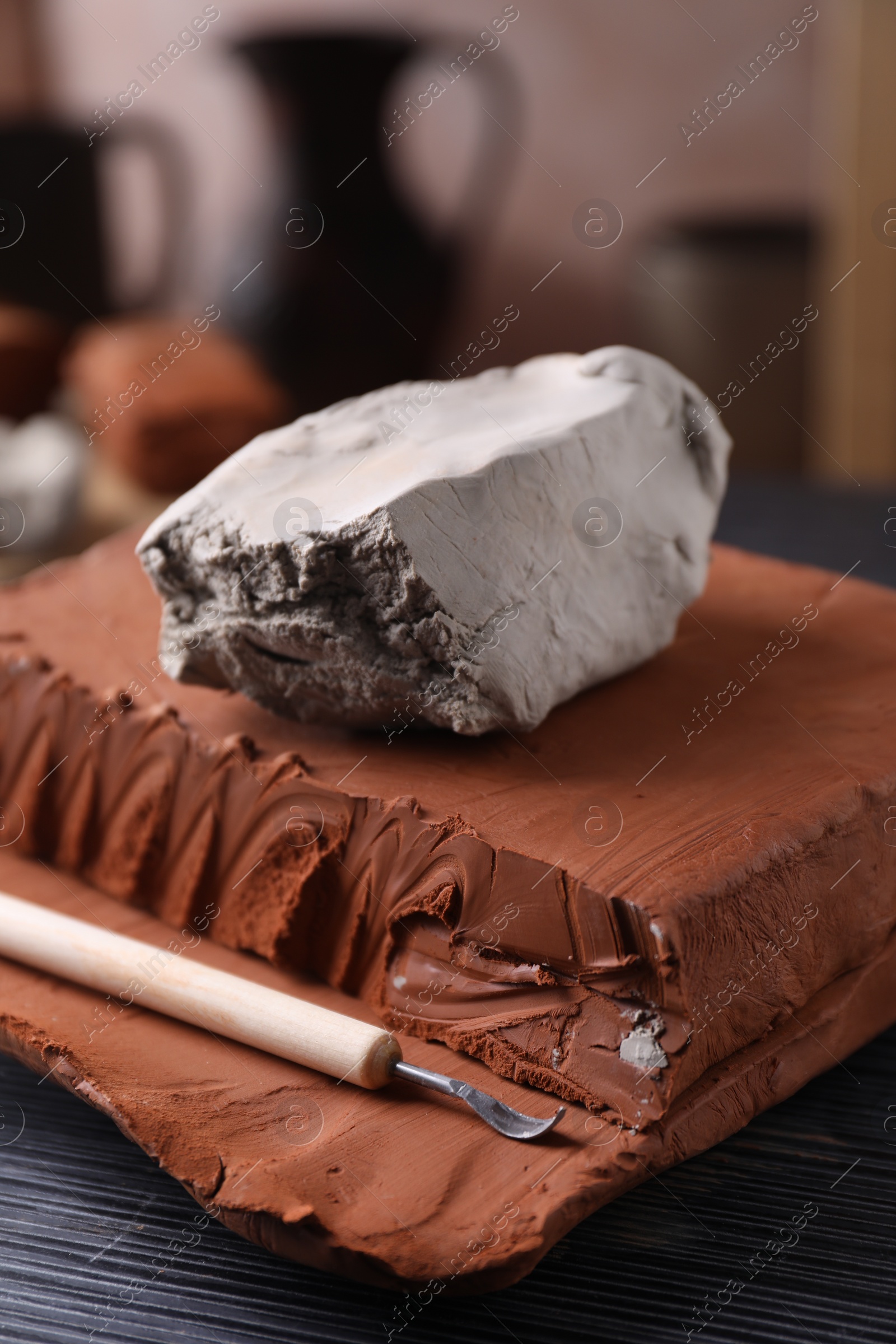 Photo of Clay and modeling tool on dark gray wooden table in workshop, closeup