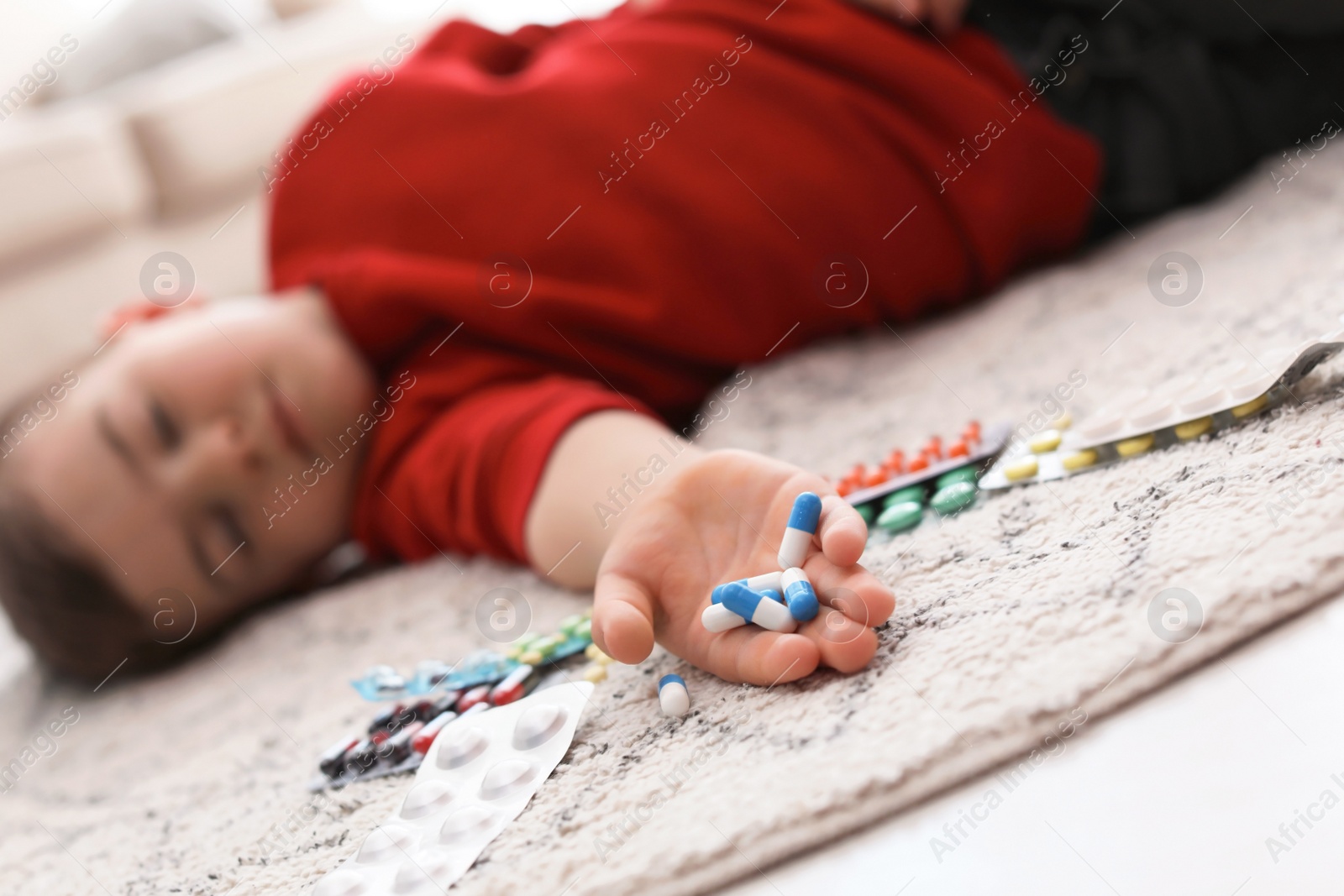 Photo of Unconscious little child with pills lying on floor at home. Household danger