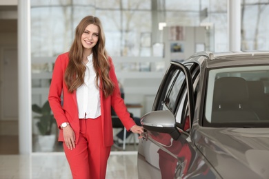 Photo of Young saleswoman near automobile in car dealership