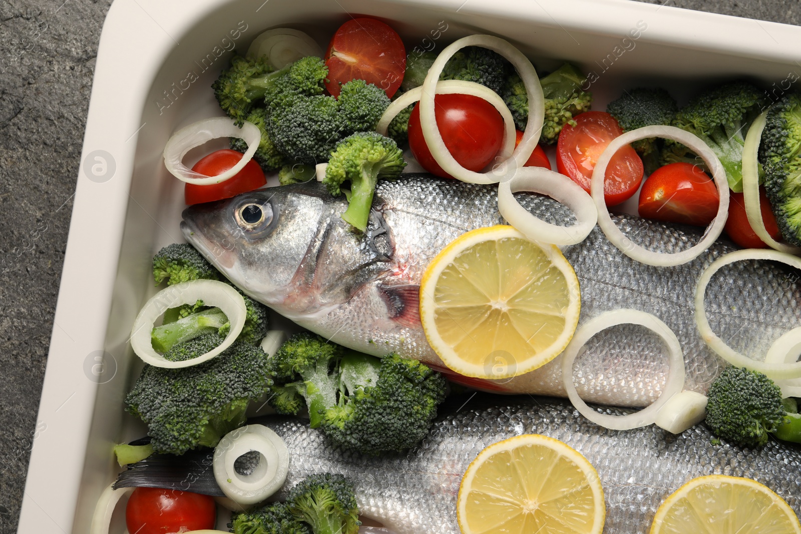 Photo of Raw fish with vegetables and lemon in baking dish on grey table, top view