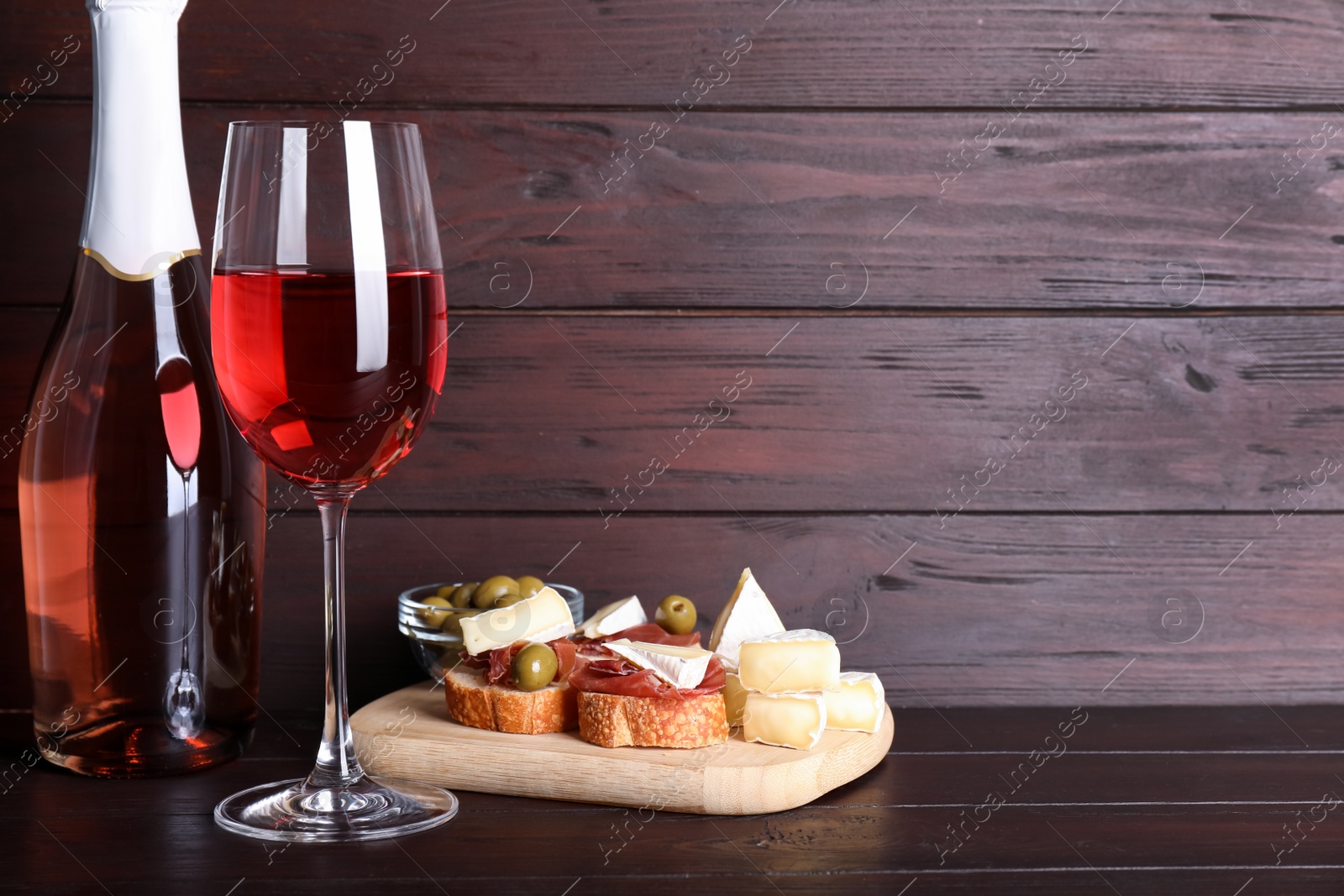 Photo of Delicious rose wine and snacks on wooden table. Space for text