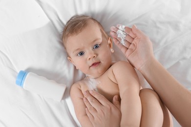 Mother applying dusting powder onto her baby on bed, top view