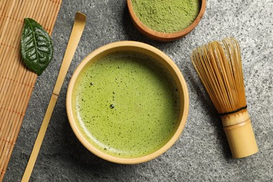 Photo of Cup of fresh matcha tea, bamboo whisk, spoon and green powder on grey table, flat lay