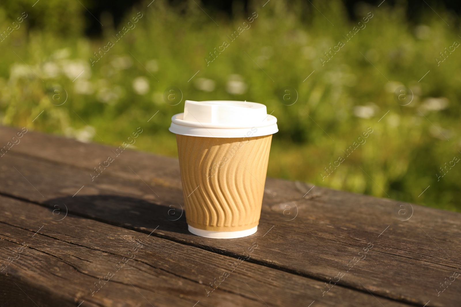 Photo of Paper cup on wooden bench outdoors. Coffee to go